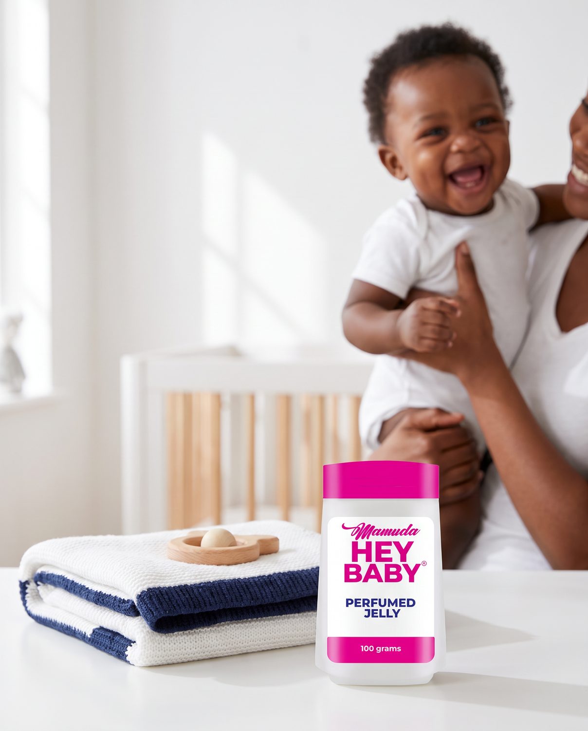 The white and magenta Mamuda Hey Baby perfumed jelly bottle large in the foreground beside a knitted baby blanket, with a laughing baby softly out of focus behind