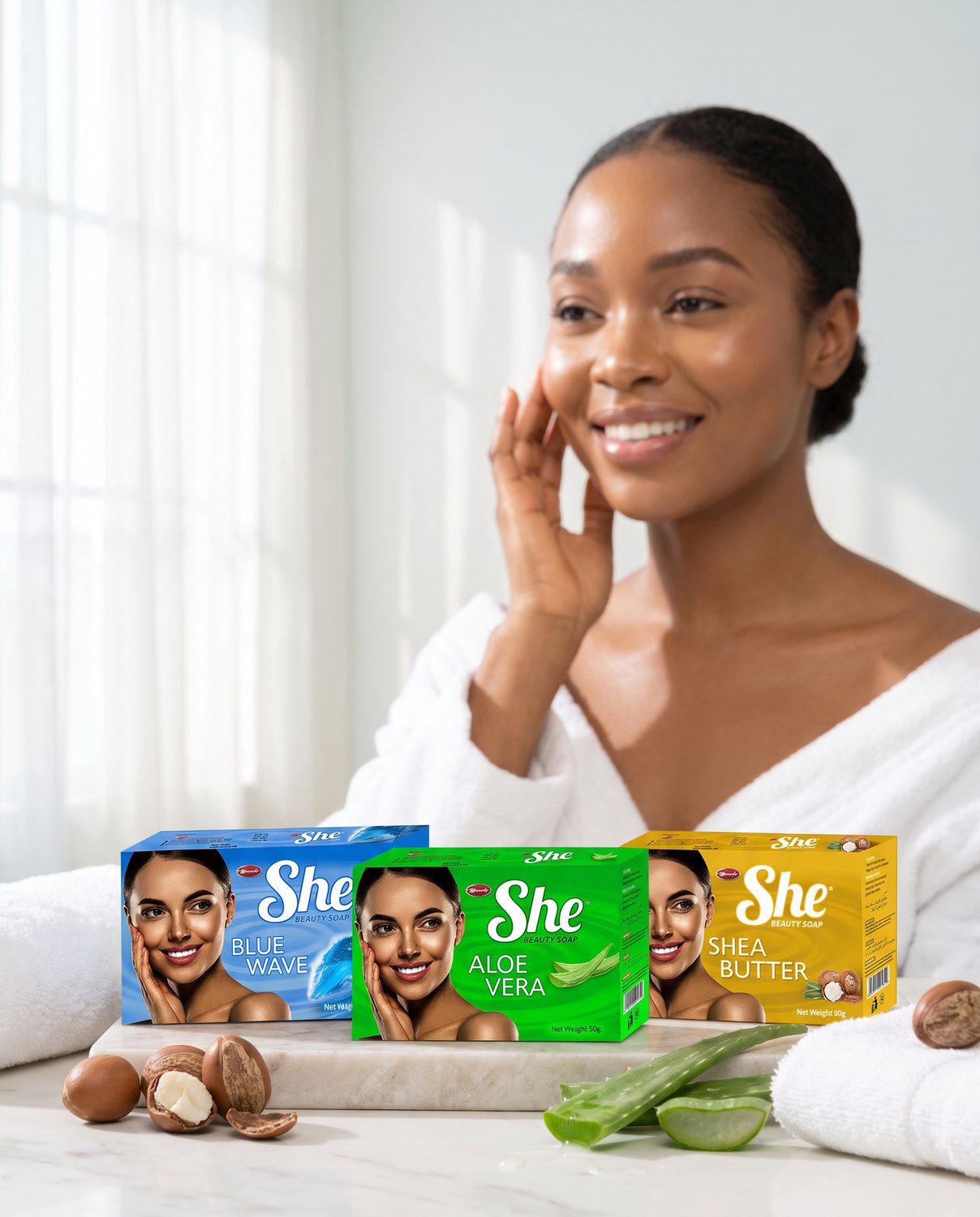 A Nigerian woman with radiant skin in a bright bathroom, with the She Blue Wave, Aloe Vera and Shea Butter beauty soap cartons grouped on the counter beside shea nuts and a cut aloe leaf
