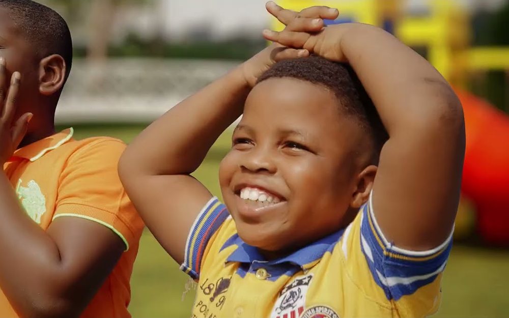 Two laughing Nigerian children playing outdoors in bright clean clothes